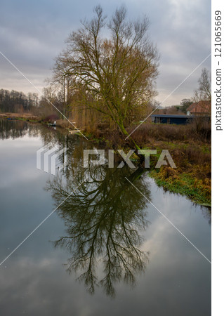A tree gives a beautiful reflection in a river. A dark sky with clouds in the background 121065669