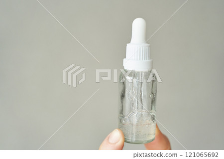 Clear dropper bottle with serum held by caucasian female hand against a neutral Clear dropper bottle with serum held by caucasian female hand against a neutral 121065692