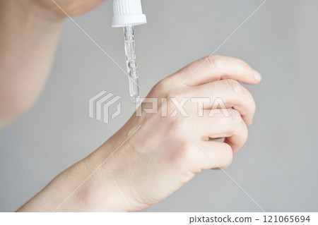 Close up of female hand applying skincare serum with dropper on light background 121065694