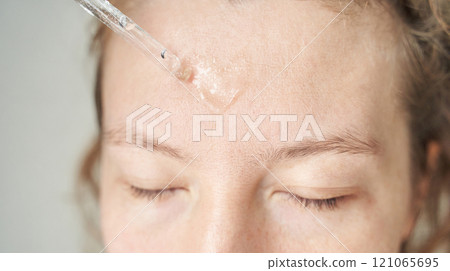 Close up of caucasian female using serum pipette on forehead for skincare 121065695