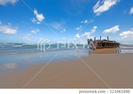 Shipwreck on Fraser Island with waves, sandy beach, and vibrant blue sky 121065890