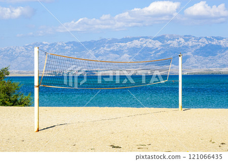 A public beach volleyball court with a net against the backdrop of sea, mountains and blue sky 121066435