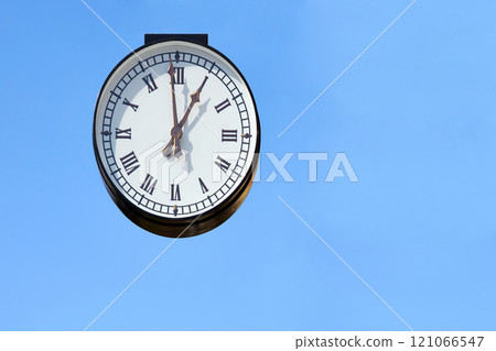 Street clock with Roman numerals, blue clear sky Street clock with Roman numerals, blue clear sky 121066547