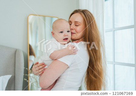 Happy family at home. Mother holding little toddler child daughter. Mom and baby girl relax playing having fun together at home. Mother hugs baby with love care. Mom of breast feeding baby 121067169