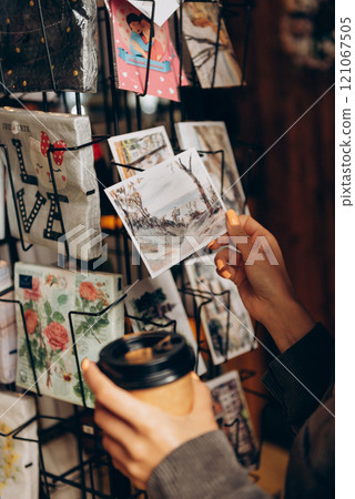 A person holds a coffee cup in front of a postcard display 121067505