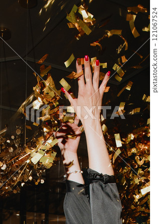 A woman with red nails joyfully tosses gold confetti in the air A woman with red nails joyfully tosses gold confetti in the air 121067524