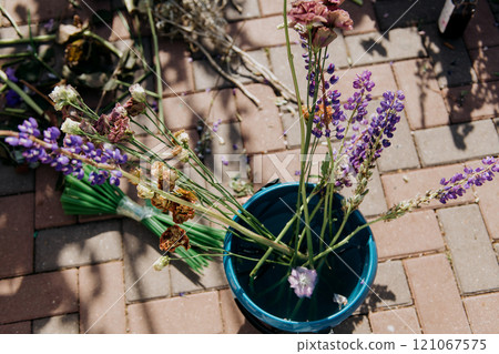 A blue pot with purple flowers sits on a brick floor 121067575