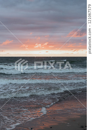 A sunset over the ocean with waves gently crashing on the beach 121067579
