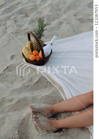 A woman relaxes on the sunny beach with a fruit basket beside her A woman relaxes on the sunny beach with a fruit basket beside her 121067653
