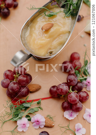 A spoon of sauce surrounded by grapes and flowers on a table 121067806