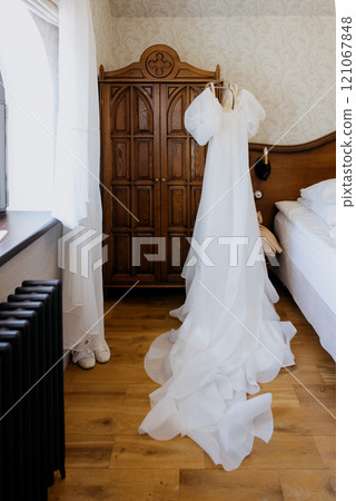 A lovely wedding dress hangs in a bedroom, creating serenity A lovely wedding dress hangs in a bedroom, creating serenity 121067848
