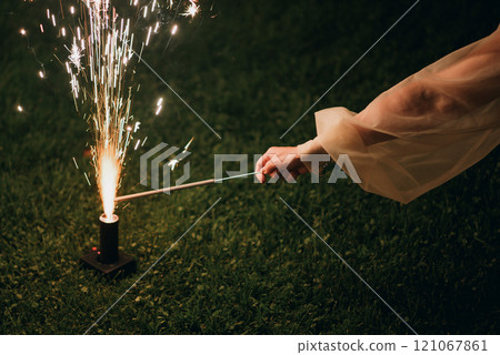 A woman joyfully holds a sparkler before a vibrant fireworks display 121067861