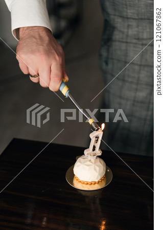 A man is using a screwdriver to light a candle on a cake 121067862