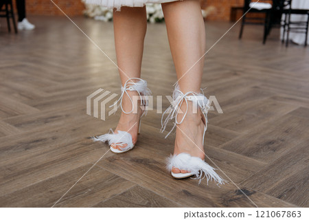 A woman in white feathered heels stands on a wooden floor 121067863