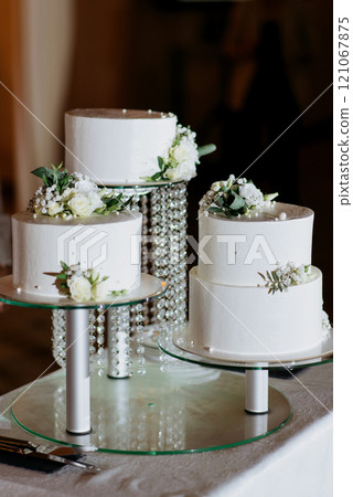 Three beautifully decorated white wedding cakes on a glass table Three beautifully decorated white wedding cakes on a glass table 121067875