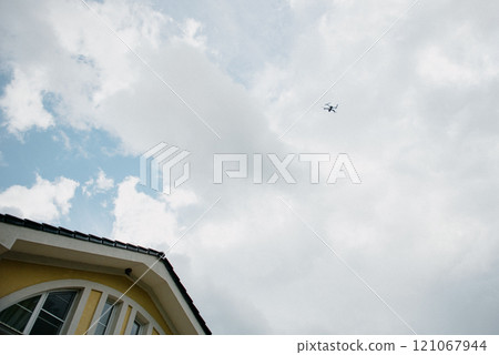 A drone is currently flying high in the sky above a yellow house 121067944