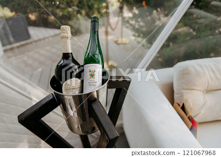 There are two bottles of wine placed inside a bucket on a table There are two bottles of wine placed inside a bucket on a table 121067968