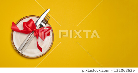 Round white plate and tied with red bow view with knife on yellow background, festive table setting Round white plate and tied with red bow view with knife on yellow background, festive table setting 121068629