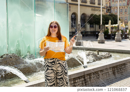 Happy 30s young female tourist is exploring new city. Woman holding a paper map on central square in Wroclaw old town in Poland. High quality photo, summer time. Vacation concept 121068837