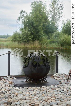 An Artistic Globe Sculpture Gracefully Placed by the Side of a Tranquil Water Body An Artistic Globe Sculpture Gracefully Placed by the Side of a Tranquil Water Body 121069954