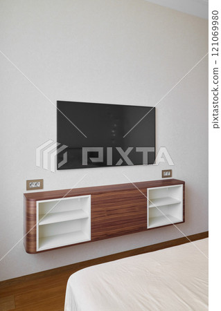 A modern bedroom designed with a wallmounted television and a stylish, sleek storage unit 121069980