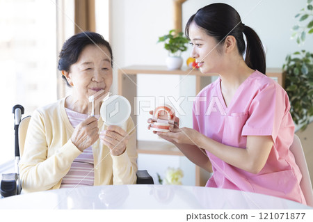 Senior woman receiving tooth brushing instruction from dental hygienist 121071877
