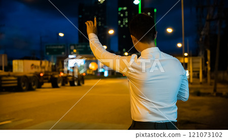Asian businessman hailing taxi at night waving hand on city road. Beautiful woman smiles uses smartphone app to call cab after late work. Twilight urban transportation scene. 121073102