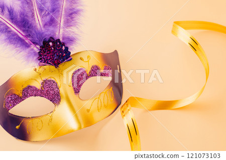 Happy Purim carnival decoration. Jewish Purim and Mardi Gras in Hebrew, Top view venetian ball mask with purple feather on pastel background, holiday background banner design, Masquerade party 121073103