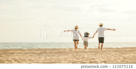 Happy Asian parents with their daughters enjoying playful at beach. Little girls with their mother and father holding hand of child running and pretending on sand. Positive family outdoor activity 121073118