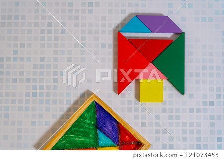 Colorful Tangram puzzle forming a figure with its container on a wooden table. Colorful Tangram puzzle forming a figure with its container on a wooden table. 121073453