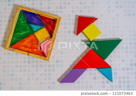 Colorful Tangram puzzle forming a figure with its container on a wooden table. Colorful Tangram puzzle forming a figure with its container on a wooden table. 121073463