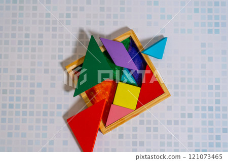 Colorful Tangram puzzle with its messy container on a wooden table. Colorful Tangram puzzle with its messy container on a wooden table. 121073465