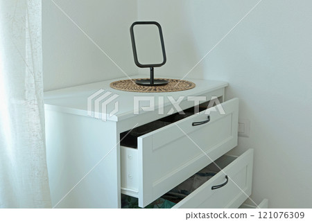 White bedroom dresser with table mirror near window. Furniture and interior in Scandinavian style. Copy space for design.  121076309