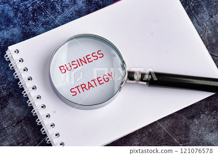 Business planning concept. BUSINESS STRATEGY on a blank page of a notebook through a magnifying glass close-up 121076578