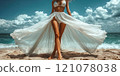 A beautiful female tourist in a light white dress walks along the beach. 121078038