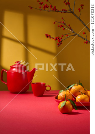 A close-up of a crimson tabletop with an empty space for product display, a red teapot, a red dish of tangerines, and a winterberry above against a golden backdrop. idea for the Chinese New Year. 121078318