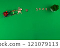 A wooden deer with branchy antlers is carrying a green wooden sleigh on which lies a red festive New Year's bow, in front of the deer there is a wooden snowflake and it is written 2025, in the corner 121079113
