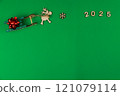 A wooden reindeer with branchy antlers is pulling a green wooden sleigh on which a red festive New Year's bow lies, a wooden snowflake lies in front of the deer and the year 2025 is written with space 121079114