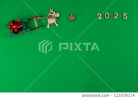 A wooden reindeer with branchy antlers is pulling a green wooden sleigh on which a red festive New Year's bow lies, a wooden snowflake lies in front of the deer and the year 2025 is written with space 121079114