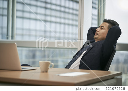 asian businessman thinking in office with hands behind head asian businessman thinking in office with hands behind head 121079626