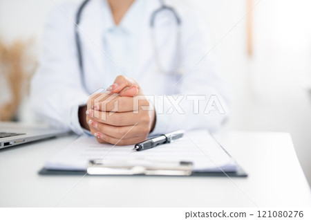 A doctor sitting at her desk with her hands clasped together, displaying a serious expression. A doctor sitting at her desk with her hands clasped together, displaying a serious expression. 121080276