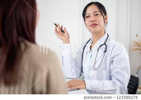 A doctor working in the examination room, listening to a patient describing their symptoms. A doctor working in the examination room, listening to a patient describing their symptoms. 121080278
