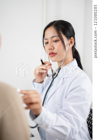 A doctor using a stethoscope to listen to a patient's lung and heartbeat sounds. A doctor using a stethoscope to listen to a patient's lung and heartbeat sounds. 121080285