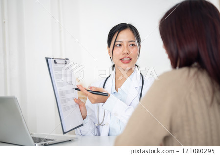 A doctor showing a medical paper to a patient while discussing the treatment plan at the hospital. A doctor showing a medical paper to a patient while discussing the treatment plan at the hospital. 121080295
