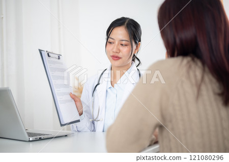 A doctor showing a medical paper to a patient while discussing the treatment plan at the hospital. A doctor showing a medical paper to a patient while discussing the treatment plan at the hospital. 121080296