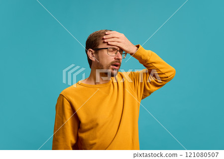 Portrait of young man dressed casually posing, holding hands on head as he feeling headache, fever against turquoise background. 121080507