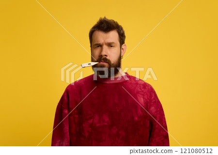 Portrait of young man with beard, with thermometer in mouth, measuring temperature against bright yellow background. Viruses and symptoms. 121080512