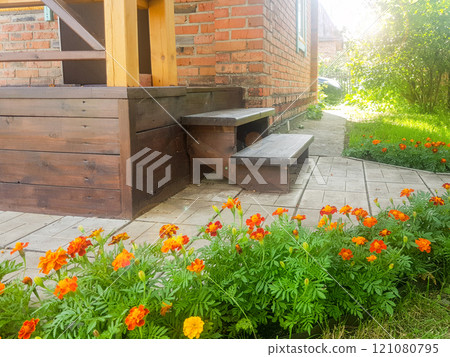Close-up of a brown wooden porch with steps near a red brick wall in a rustic country house, on a sunny summer day 121080795