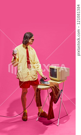 Combining retro tech with casual office wear, this man enjoys coffee break while handling household tasks, merging different aspects of office life. 121081384