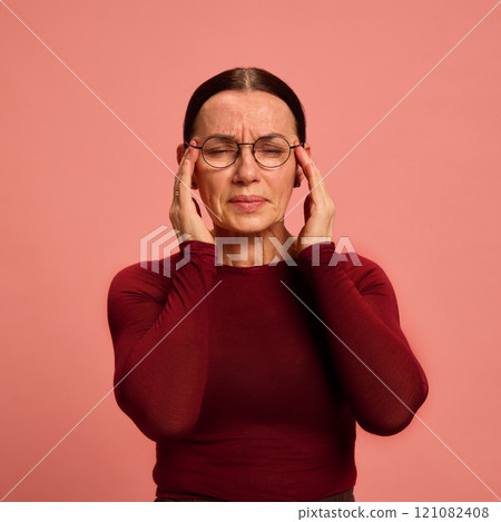 Senior woman holding hand on head, feeling pain against pastel peach background. Symptoms and treatments. Stress. 121082408